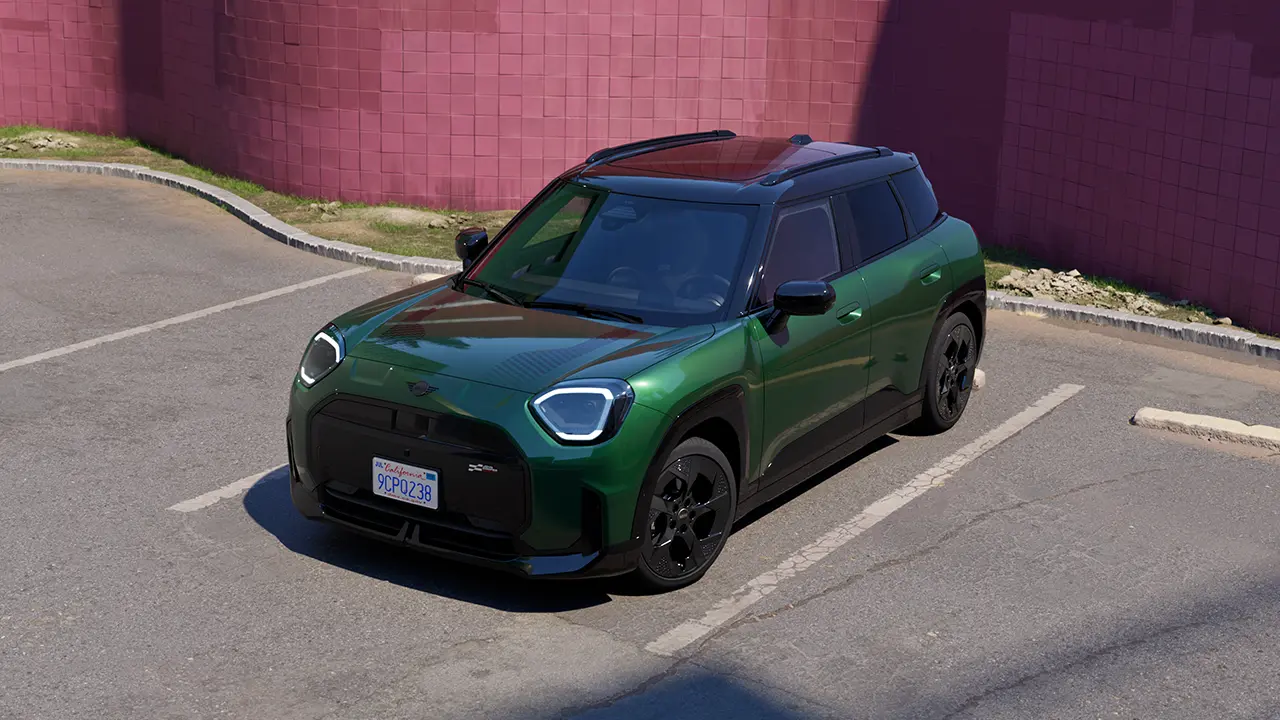 Prednji prikaz potpuno električnog MINI Aceman-a British Racing zelene boje na parkingu sa ružičastim zidom u pozadini