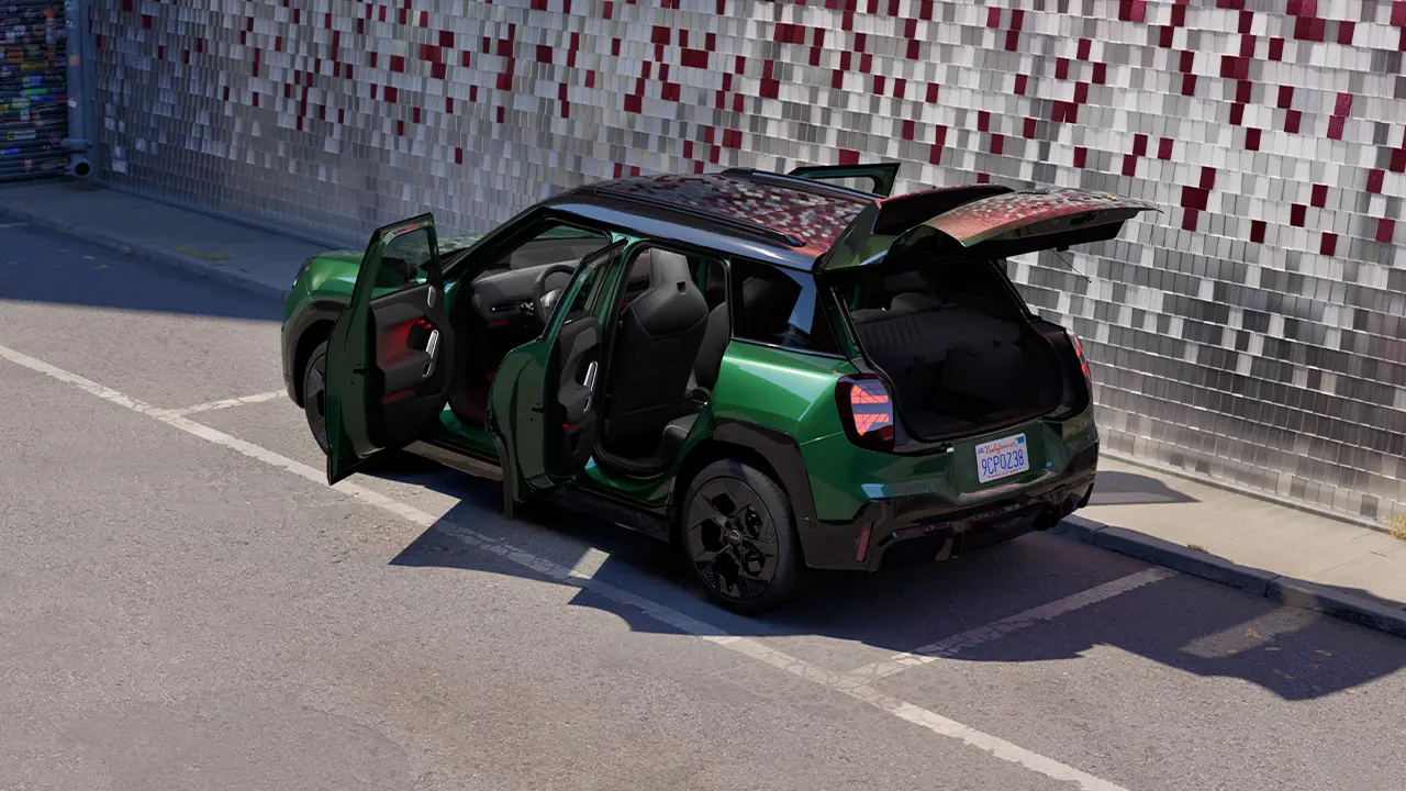 Prikaz zadnje strane potpuno električnog MINI Aceman-a British Racing zelene boje na parkingu sa otvorenim vratima i obojenim zidom u pozadini