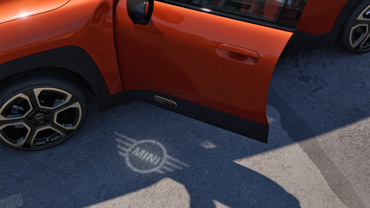 Spoljašnji prikaz potpuno električnog MINI Aceman-a sa otvorenim vratima i MINI svetlom dobrodošlice sa projekcijom logotipa na zemlji 