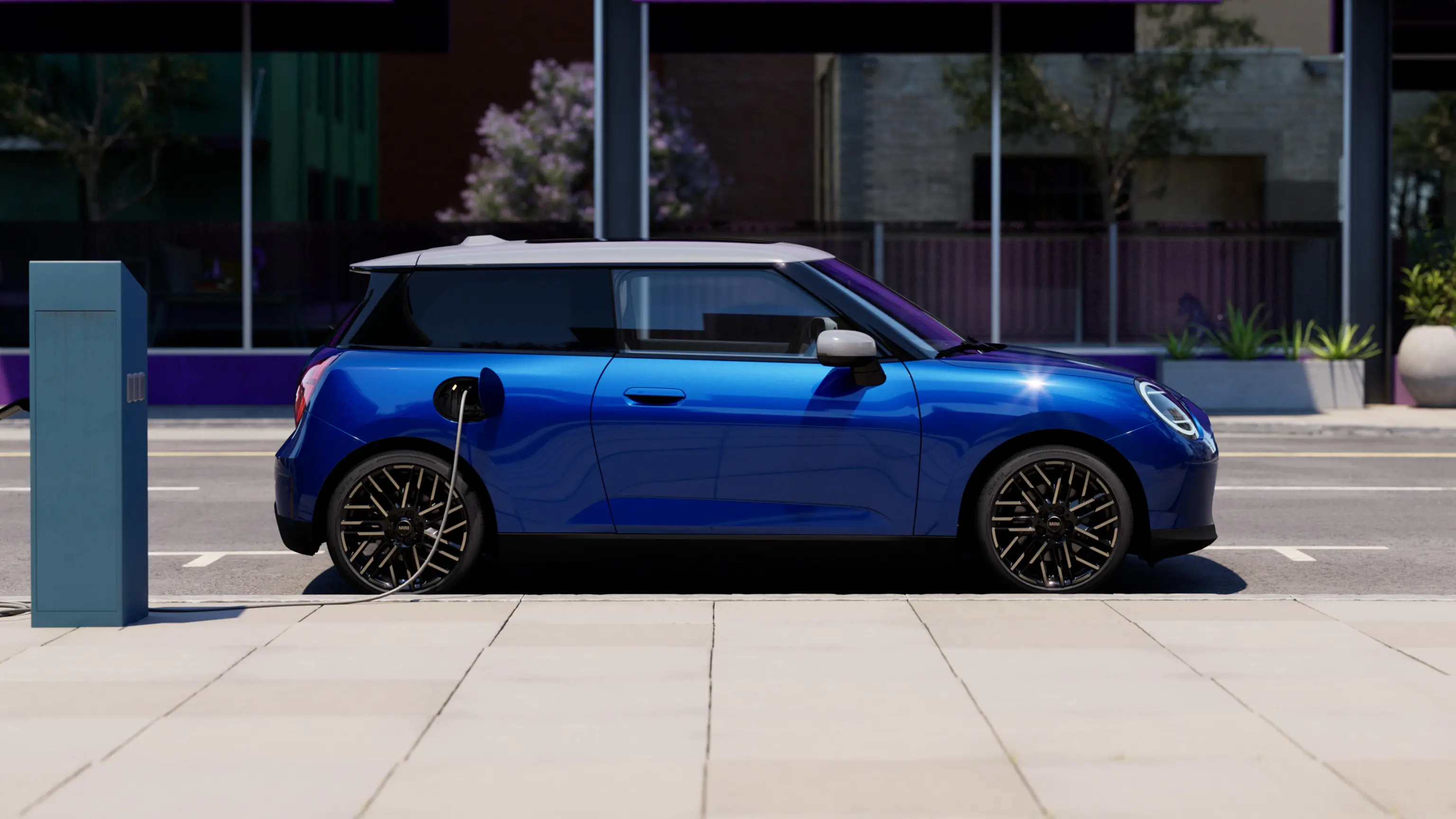 Bočni prikaz potpuno električnog MINI Cooper-a Blazing plave boje parkiran na trotoaru pored stanice za punjenje