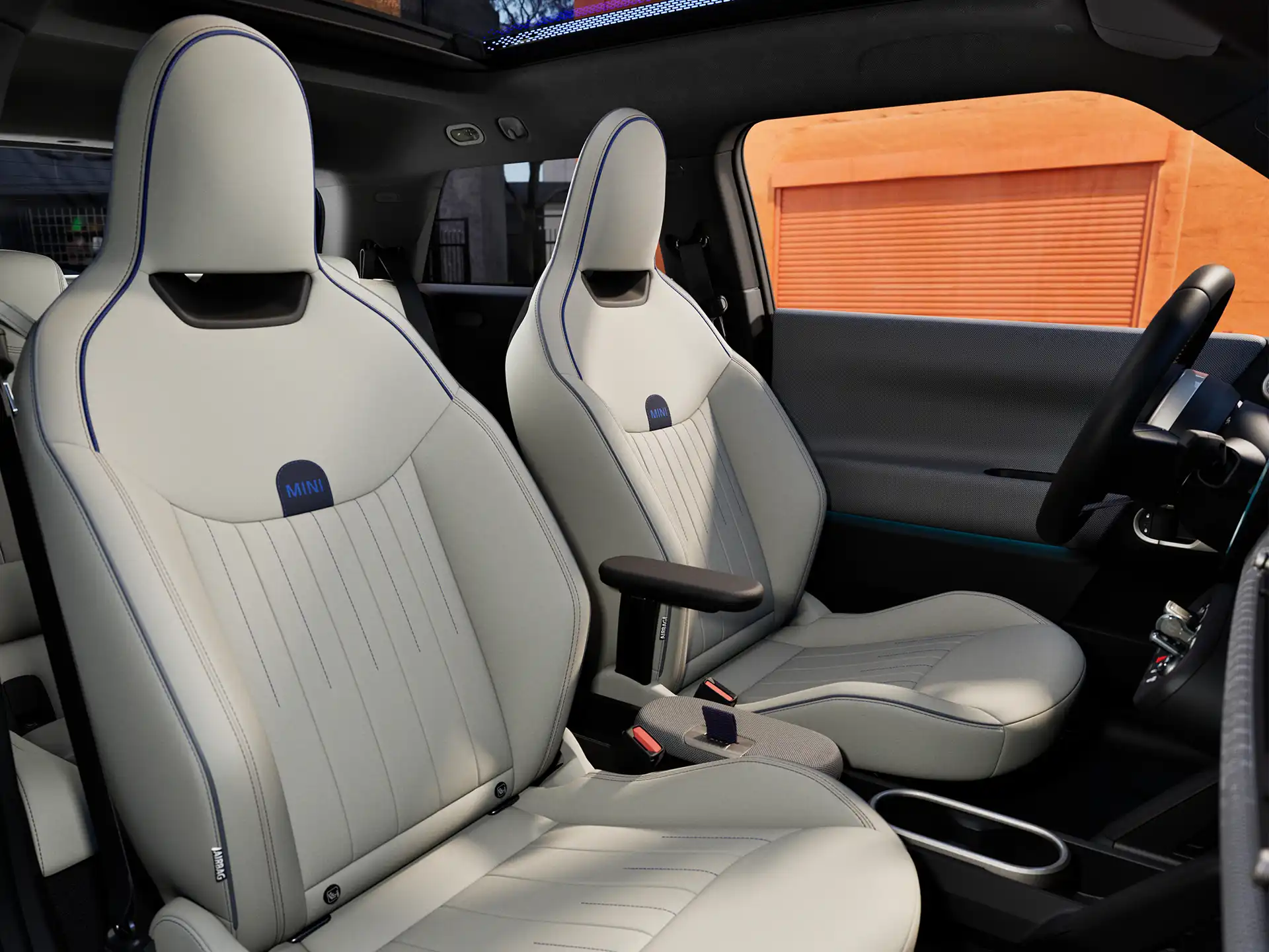 Unutrašnja perspektiva potpuno električnog MINI Cooper-a sa komandnom tablom, volanom, okruglim ekranom, panoramskim staklenim krovom i zadnjim delom prednjih sedišta.
