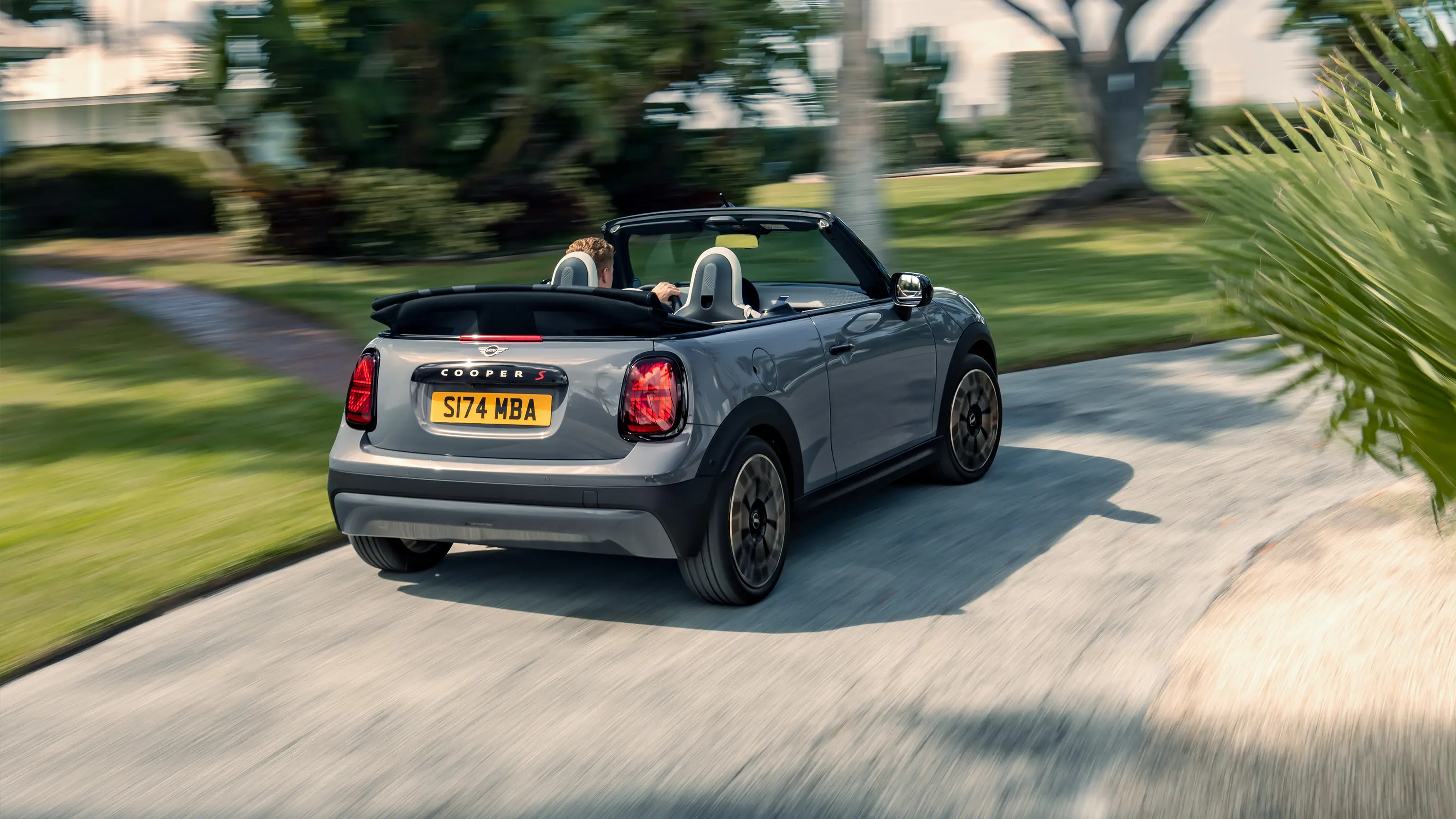 Prikaz MINI Cooper Kabrioleta Copper sive boje otpozadi prilikom vožnje ulicom 