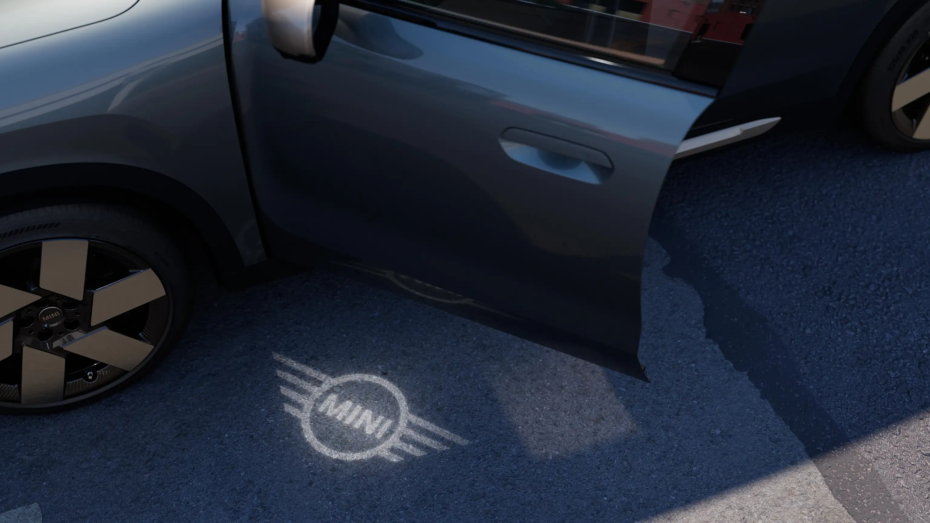 Spoljašnji prikaz potpuno električnog MINI Countryman-a sa otvorenim vratima i MINI svetlom dobrodošlice sa projekcijom logotipa na zemlji 