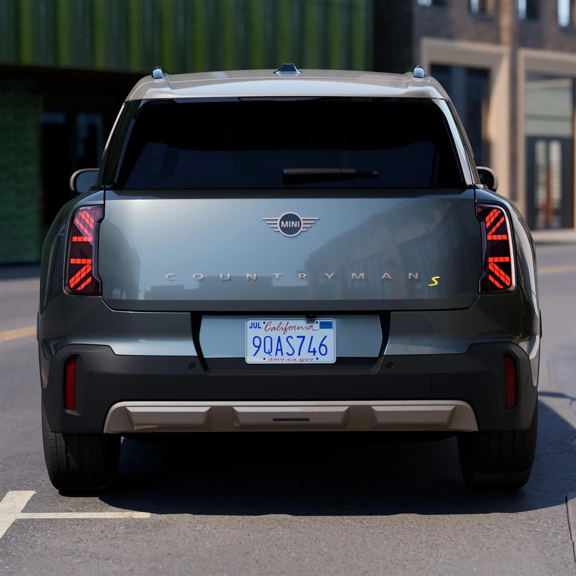 Prikaz zadnje strane potpuno električnog MINI Countryman-a Smokey zelene boje sa živahnim srebrnim krovom tokom parkiranja