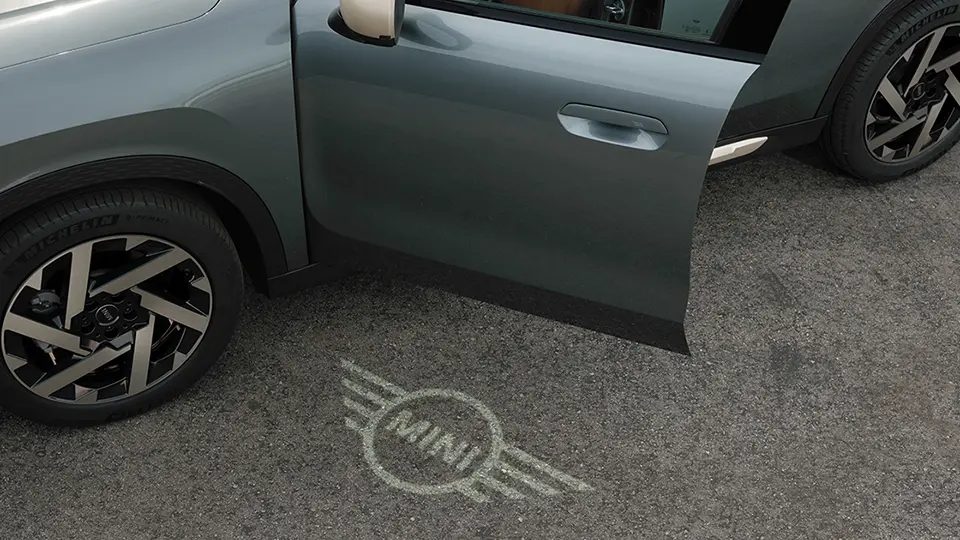 Spoljašnji prikaz MINI Countryman-a sa otvorenim vratima i MINI svetlom dobrodošlice sa projekcijom logotipa na zemlji