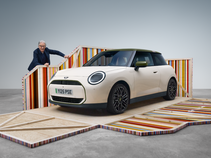 Pogled spreda sa strane na potpuno električni MINI Cooper Paul Smith izdanje u boji Inspired White, pored kog stoji dizajner Paul Smith.